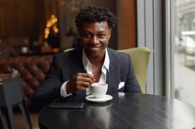 Bir kafede oturan ve kahve içen siyah bir adam.
