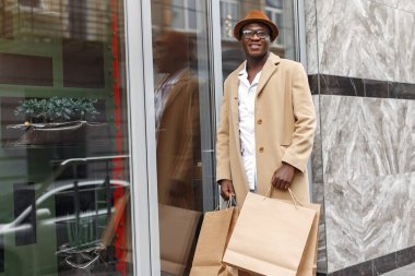 Alışveriş torbalarıyla dolu bir şehirde şık bir zenci.