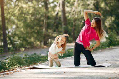 Anne ve kızı yaz parkında yoga yapıyor.