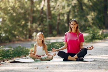Anne ve kızı yaz parkında yoga yapıyor.