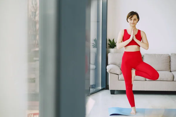 Дівчина в червоній спортивній формі робить йогу вдома — стокове фото
