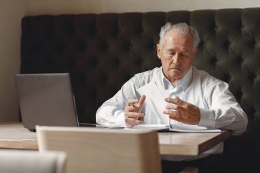 Yaşlı adam masada oturuyor ve dizüstü bilgisayarla çalışıyor.