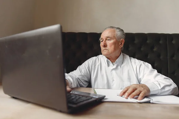 老人坐在桌旁，拿着笔记本电脑工作 — 图库照片