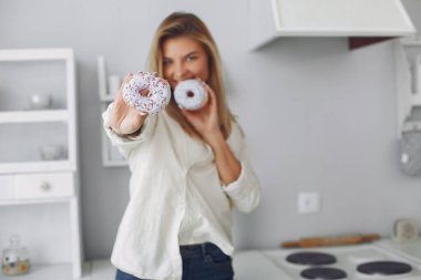 Güzel bir kız mutfakta donutla duruyor.