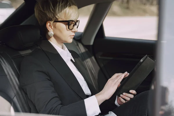 Empresaria sentada dentro de un coche y usando una tableta — Foto de Stock