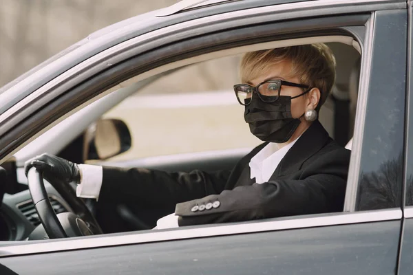 Mujer de negocios con una máscara negra sentada dentro de un coche — Foto de Stock