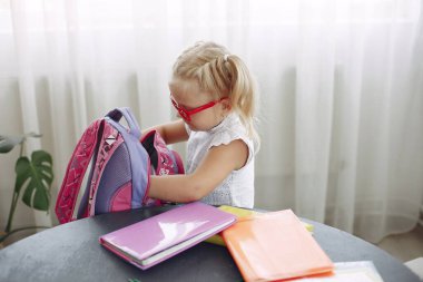 Kitaplarla dolu bir masada oturan küçük kız.