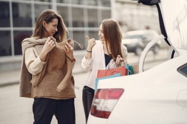 Alışveriş torbalarıyla arabanın yanında duran kadın.