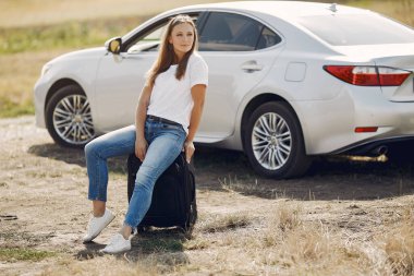 Arabanın yanında bavullu zarif bir kadın.