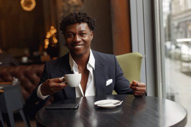 Bir kafede oturan ve kahve içen siyah bir adam.