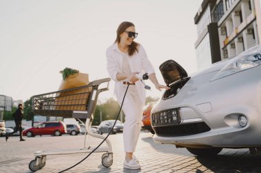 Elektrikli benzin istasyonunda kadın elektro arabayı şarj ediyor.