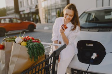 Elektrikli benzin istasyonunda kadın elektro arabayı şarj ediyor.