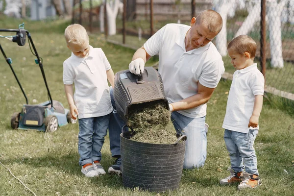 Cortacésped hombre trabajando en el patio trasero con hijos —  Fotos de Stock