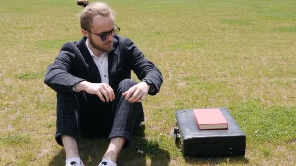 Empresario con libro sentado en una ciudad de verano — Vídeo de stock