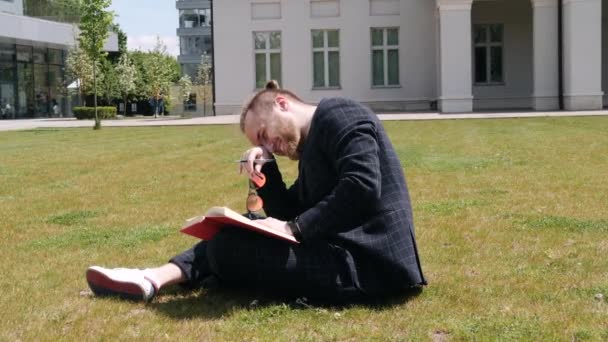 Zakenman met boek zittend in een zomerstad — Stockvideo