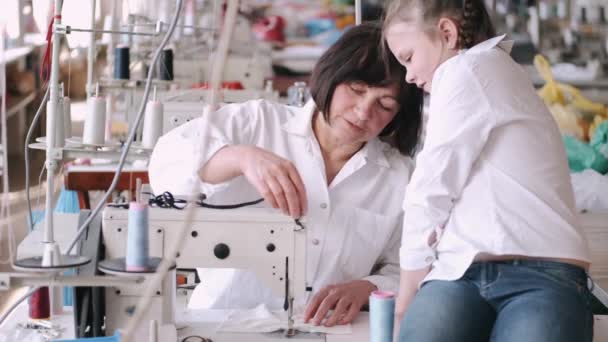 Mormor med lilla barnbarn syr kläder i fabriken — Stockvideo