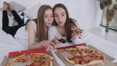 Kız arkadaşlar pizza yer ve evde televizyon izlerler.