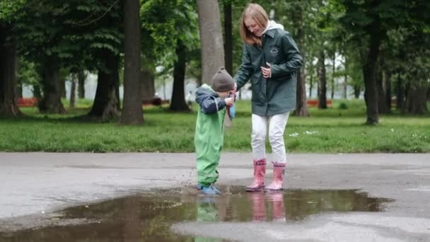 Chico divertido con botas de lluvia jugando en un parque de lluvia — Vídeo de stock