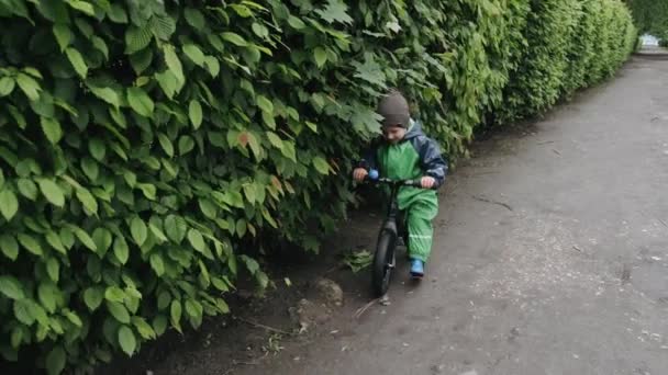 Vtipné dítě v dešti boty hrát v deštném parku — Stock video