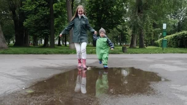 Vtipné dítě v dešti boty hrát v deštném parku — Stock video