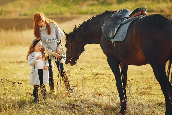 Mor och dotter på ett fält leker med en häst — Stockfoto