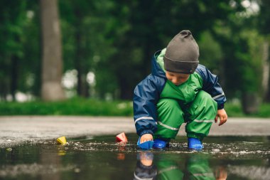 Yağmur parkında oynayan çizmeli komik çocuk.