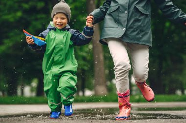 Yağmur parkında oynayan çizmeli komik çocuk.