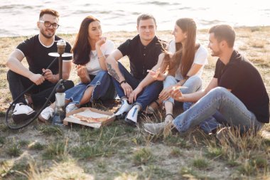 Dışarıda pizza yiyen gençler sigara içiyorlar.