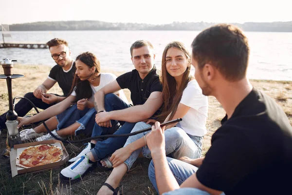 Young people eating pizza smoking shisha outside