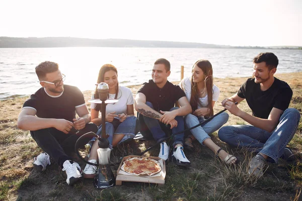 Young people eating pizza smoking shisha outside