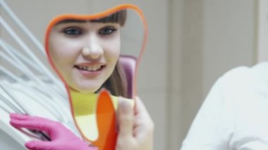 Güzel bir kız dişçilerin aynasına bakıyor.