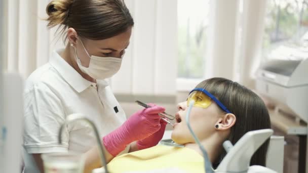 Dentystka w masce leczy pacjenta w specjalnych okularach. — Wideo stockowe