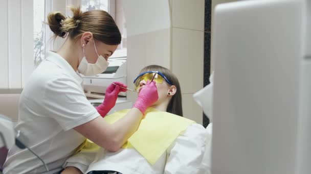 Zubařka v masce léčí pacienta ve speciálních brýlích — Stock video