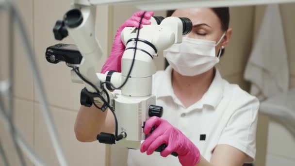 En kvinnlig endodontist behandlar kanaler under mikroskop. — Stockvideo