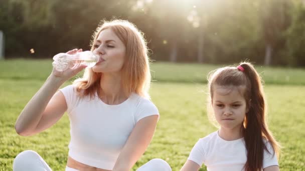 Mom and girl are sitting on the lawn and listening to music — Stock Video