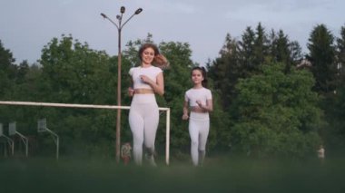 Kadın ve kızı parkta birlikte koşuyorlar.