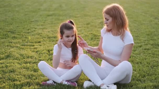 Krásná matka a dcera poslouchají hudbu na trávníku — Stock video