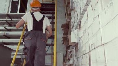 Depo işçisi elinde bir kutuyla merdivenden yukarı çıkıyor.