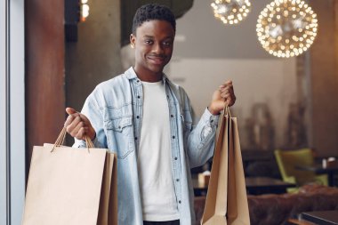 Bir kafede elinde poşetlerle duran siyah bir adam.