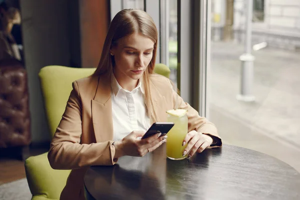 Елегантна жінка сидить за столом з коктейлем і телефоном — стокове фото