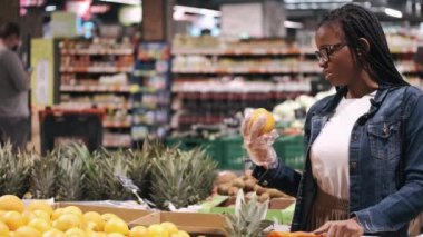 Siyah genç bir kadın süpermarkette portakal seçiyor.