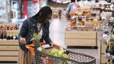 Afrikalı bir kız süpermarkette el arabasında ürünleri kontrol ediyor.