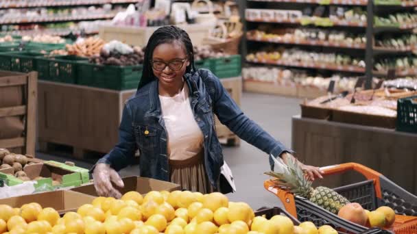 A fekete fiatal nő narancsot választ egy szupermarketben. — Stock videók