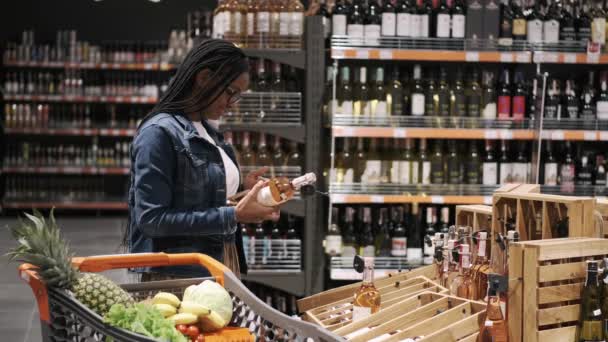 Jovencita eligiendo una botella de vino en un supermercado — Vídeos de Stock