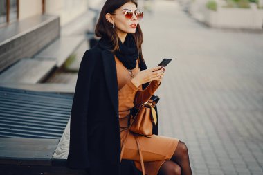 Şık bir kız telefonunu kullanarak şehirde dolaşıyor.