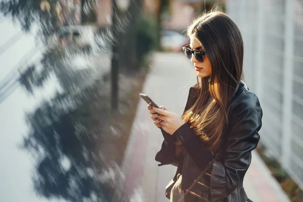 Chica elegante caminando por la ciudad mientras usa su teléfono — Foto de Stock