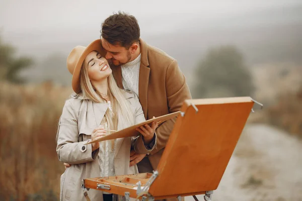 Elegant couple painting in a autumn field — Stock Photo, Image