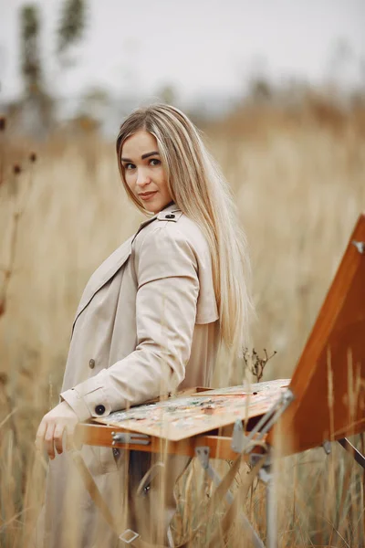 Woman in a brown coat painting in a field — Stock Photo, Image