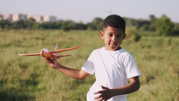 Afrikansk pojke i vit skjorta med ett plan i händerna på fältet — Stockvideo