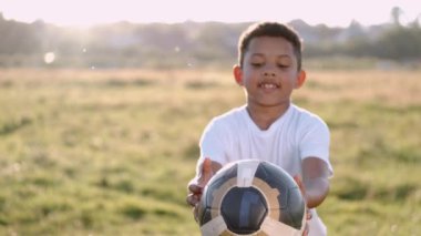Afrikalı çocuk yaz sahasında tek başına futbol oynuyor.